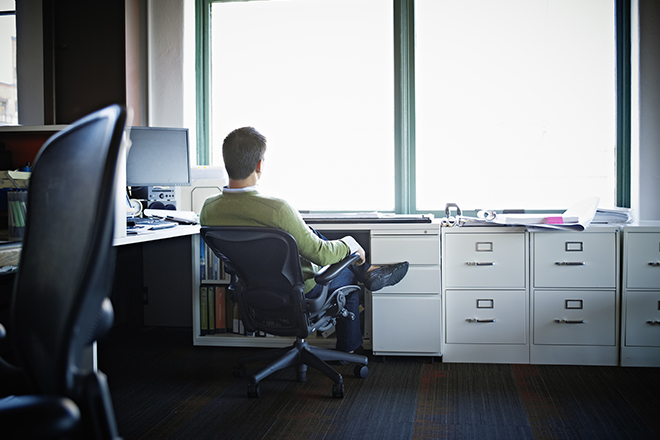 Businessman sitting in chair at office workstation looking out window rear view