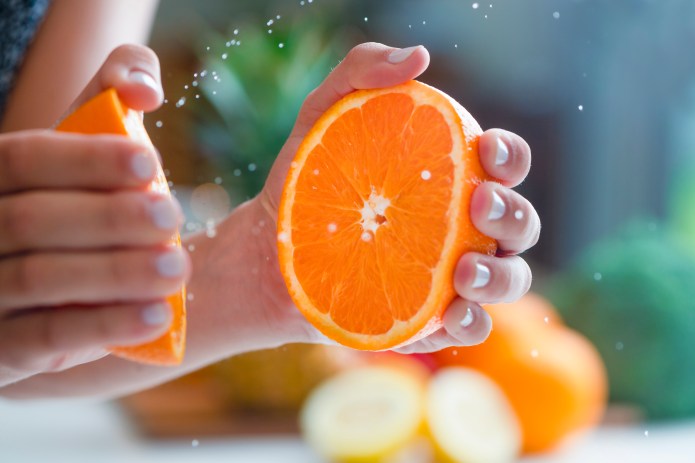 Woman squeezing the juice from an orange. Some droplets of juice can be seen. Two halves of the orange can be seen.