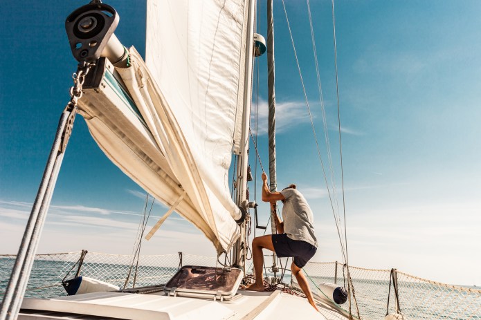 Man on sailing boat unfurling a sail in good weather