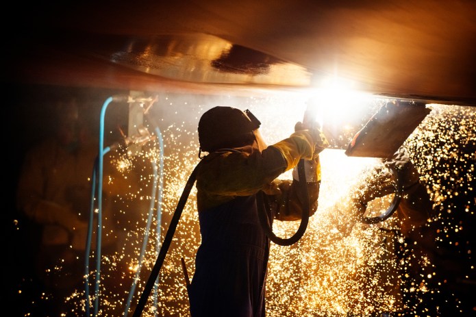 Side view of worker welding airplane wing at night